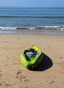a green kayak on the beach next to the water